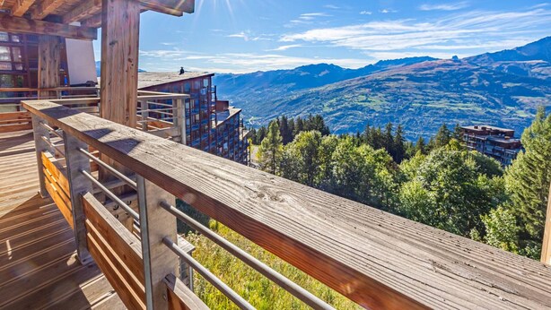 Una terraza de madera con barandilla metálica que da a un paisaje montañoso.