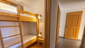 Dormitorio con literas, un taburete de madera y una lámpara de pared.