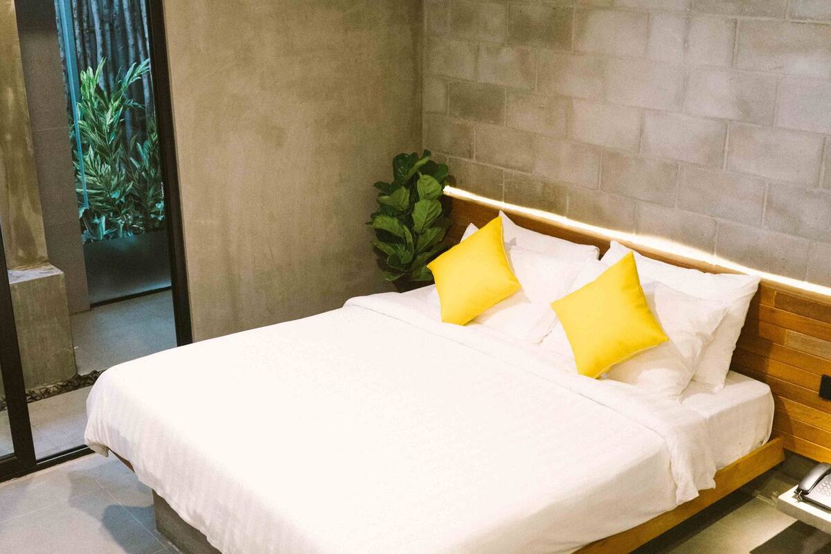 A modern bedroom with a large bed, a potted plant, and a concrete wall.