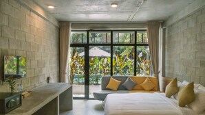 Ein modernes Hotelzimmer mit einem großen Bett, einer Sitzecke mit Kissen, einem Fernseher und Blick auf Grünflächen.