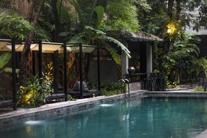 A pool area with a covered seating area, surrounded by lush greenery and a stone wall. - Larimar Hotel and Resort (Phnom Penh)