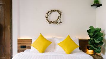 Un lit bien fait, avec une literie blanche et deux coussins jaune vif, une tête de lit en bois, une couronne décorative accrochée au mur et une plante verte posée sur une table de chevet.