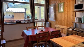 Ein Zimmer mit Holzwänden, einem Esstisch und Stühlen, einer Mikrowelle und Blick auf eine Berglandschaft durch große Fenster.