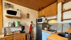 Eine kleine Küche mit Holzausstattung, einer Mikrowelle, einer Kaffeemaschine und einem Kühlschrank.