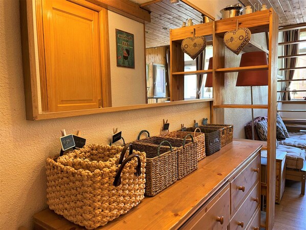 A wooden counter with woven baskets and a mirror reflecting a room with a bed and a window.