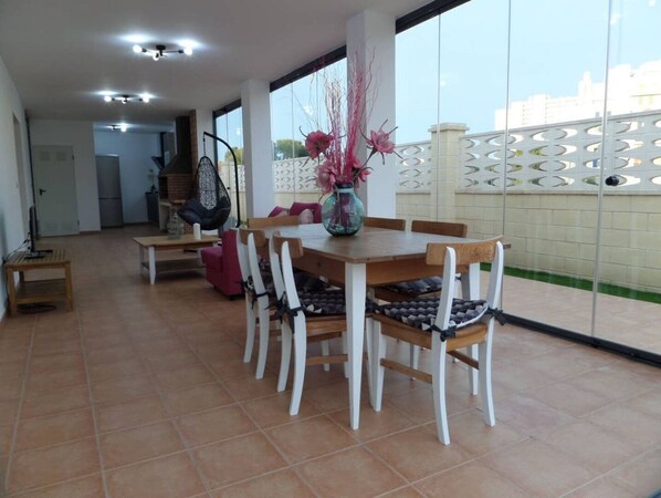 A dining area with a wooden table and chairs, a hanging chair, and a vase with flowers.