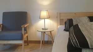 A room with a wooden chair, a small table with a lamp, and a bed with pillows. - Privatzimmer EKO 1 (Kassel)