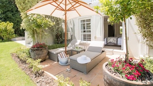 A patio with outdoor furniture, a large umbrella, and a flower bed. - 18 On Hillwood Villa (Bishopscourt)
