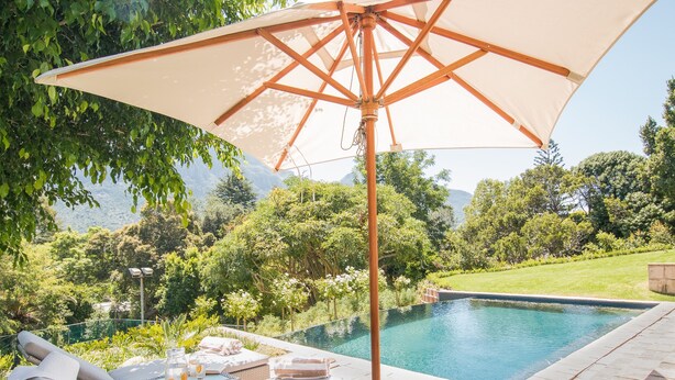 A poolside area with a lounge chair and umbrella, surrounded by lush greenery and a view of mountains. - 18 On Hillwood Villa (Bishopscourt)