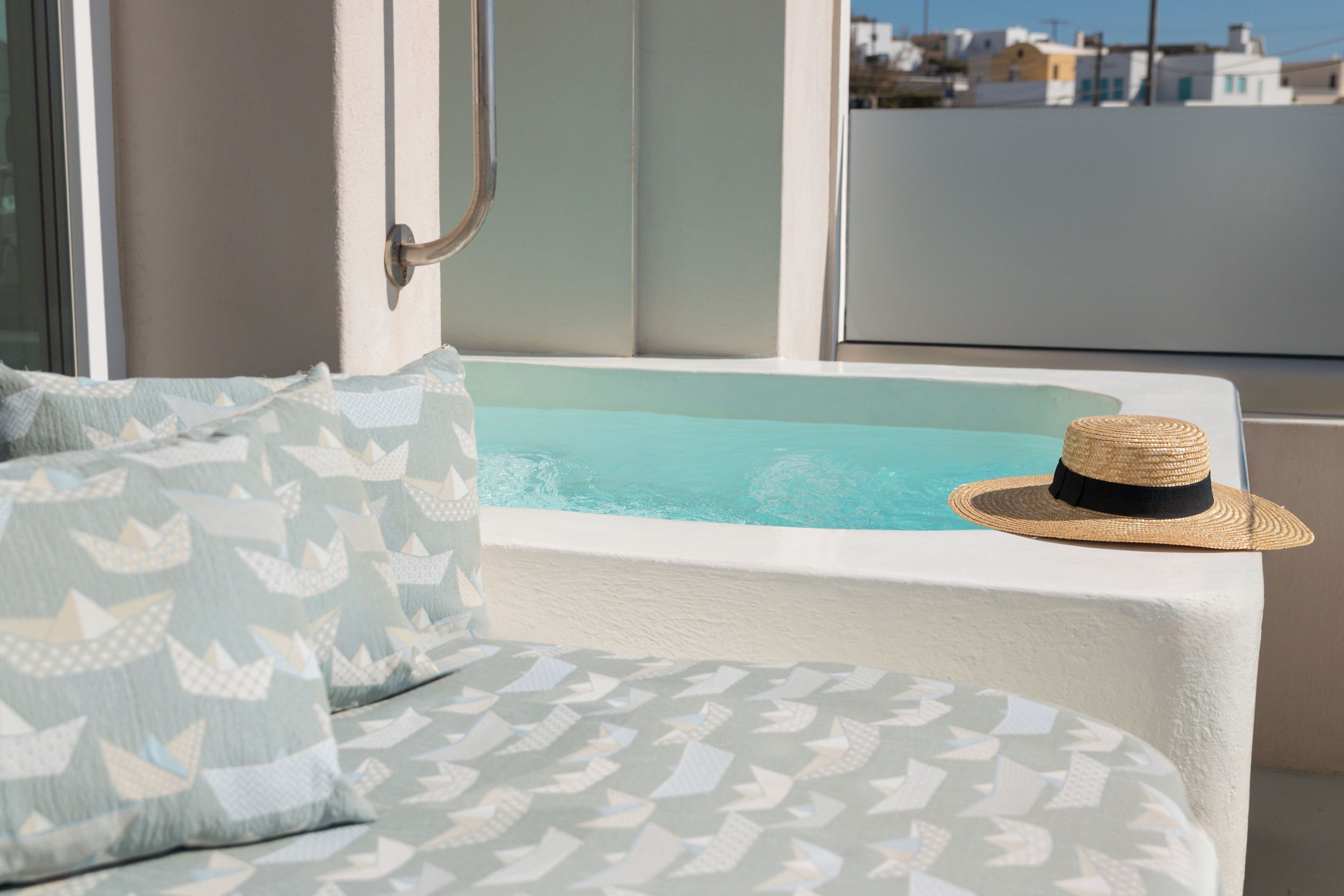A poolside area with a white tub, patterned cushions, and a straw hat on a white table.