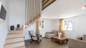 A spacious living room with a wooden staircase, a sofa, a coffee table, and a chair. - Cinnamon Villa with Private Hot Tub (Santorini)