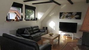 A living room with a black leather sofa, a wooden coffee table, a flat-screen TV, and a fireplace. - AhrHeim Brave new apartment on the Ahr (Bad Neuenahr)
