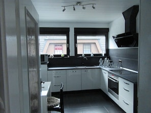 A compact kitchen with a built-in oven, a microwave, and a sink. There are two windows providing natural light, and a 'Welcome' sign above the sink.
