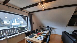 A dining area with a long table, black chairs, a bicycle, and a view of houses through a large window. - AhrHeim Brave new apartment on the Ahr (Bad Neuenahr)