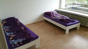 Une chambre avec deux lits simples, un plancher en bois, une fenêtre donnant sur un espace verdoyant et un radiateur.