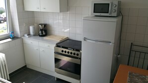 Une cuisine compacte avec des meubles blancs, un four encastré, un four à micro-ondes et une machine à café.