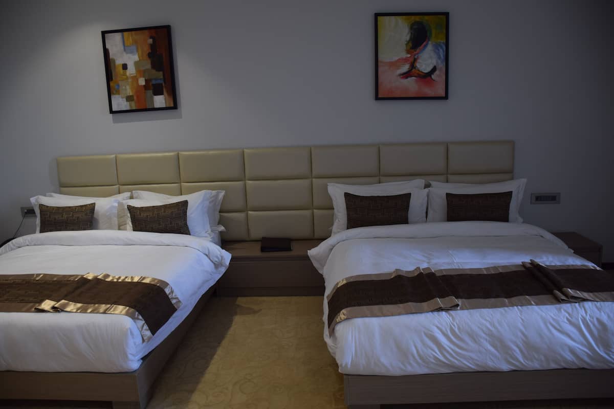 A hotel room with two beds, beige headboards, and a neutral color scheme.