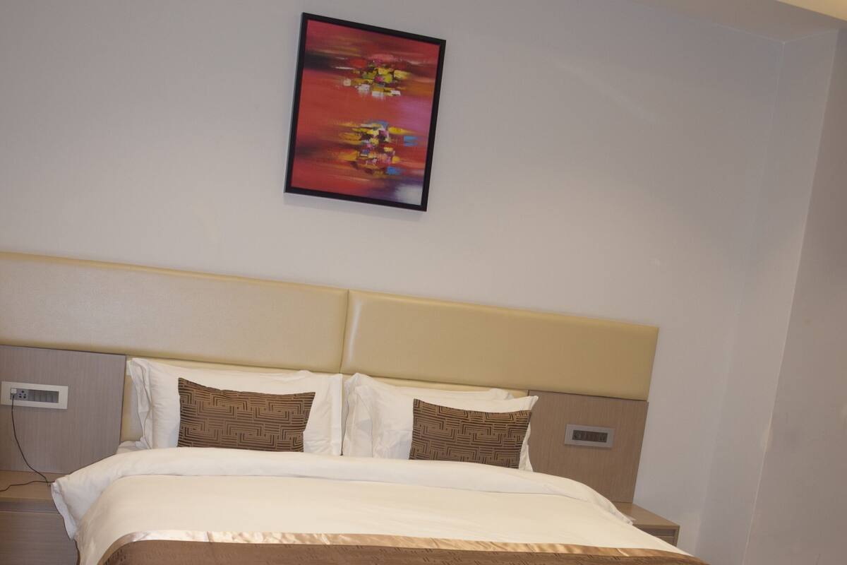 A hotel room with a large bed, headboard, and a wall-mounted painting.