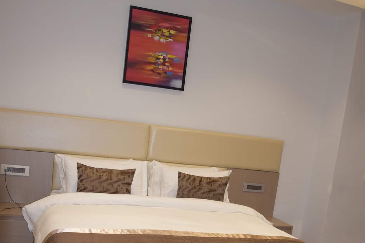 A hotel room with a large bed, a headboard, a wall-mounted painting, and a patterned carpet.