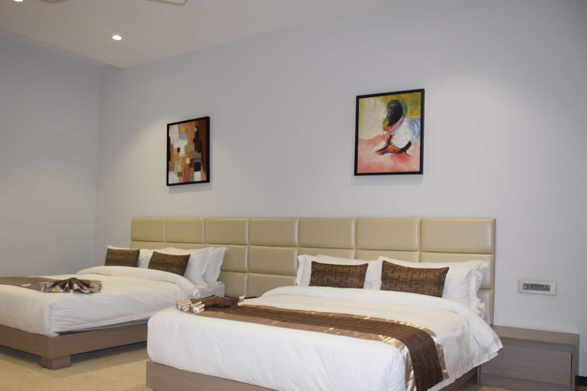 A hotel room with two beds, a beige headboard, and two framed artworks on the wall.
