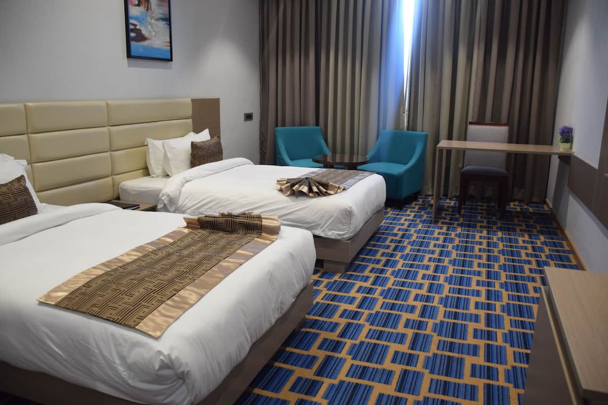 A hotel room with two beds, a desk, a chair, and a small table.