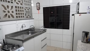 Une cuisine avec des meubles blancs, une cuisinière à gaz, un évier et une fenêtre avec des stores.