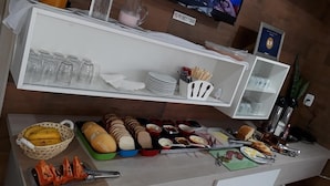 Un buffet proposant une variété de plats et d’ustensiles, un téléviseur diffusant un programme d’information et une étagère contenant de la verrerie et des assiettes.