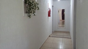 Un couloir étroit aux murs blancs, doté d’un sol carrelé, d’une fenêtre à cadre blanc et d’un extincteur rouge fixé au mur.