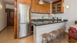 Une cuisine dotée de meubles en bois, d’un réfrigérateur en acier inoxydable, d’un comptoir en granit et d’un coin bar avec des tabourets.