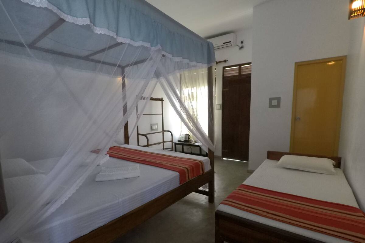 A room with two single beds, each with a canopy, a small table with a cup, and a door.