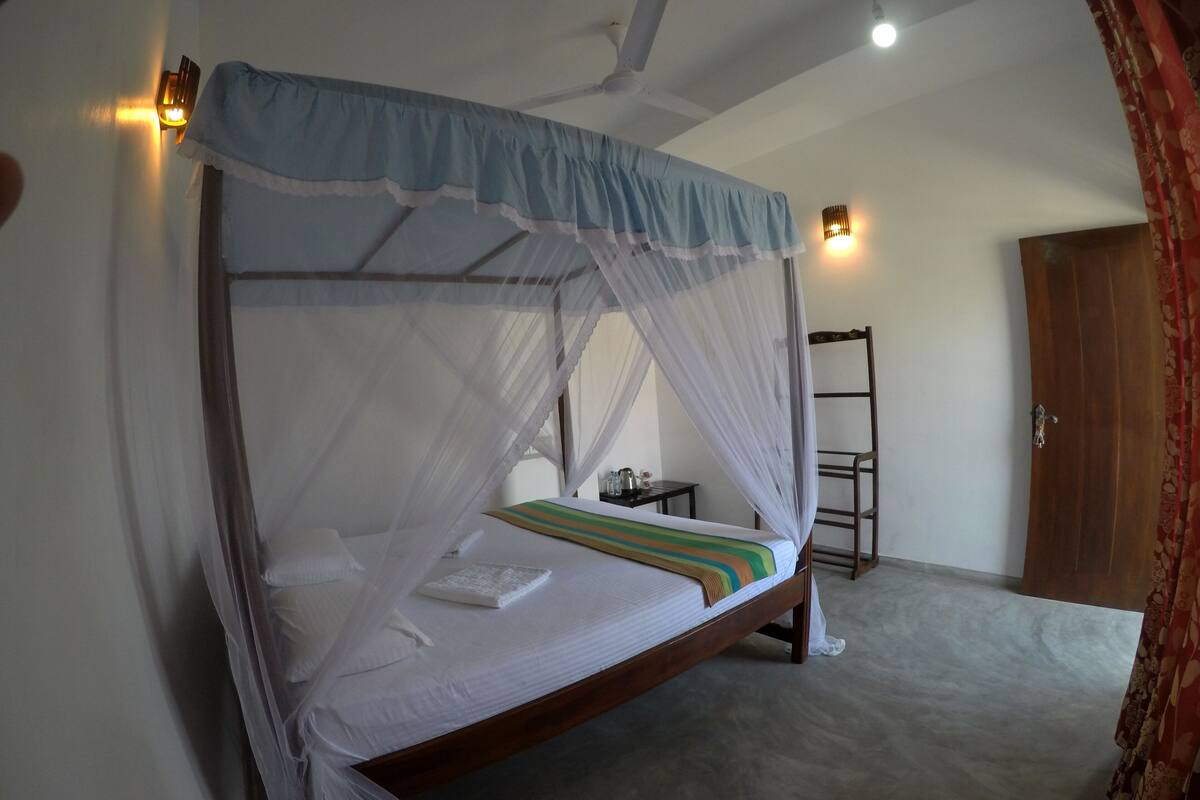 A single bed with a canopy, a small table with a lamp, and a wooden ladder against the wall.