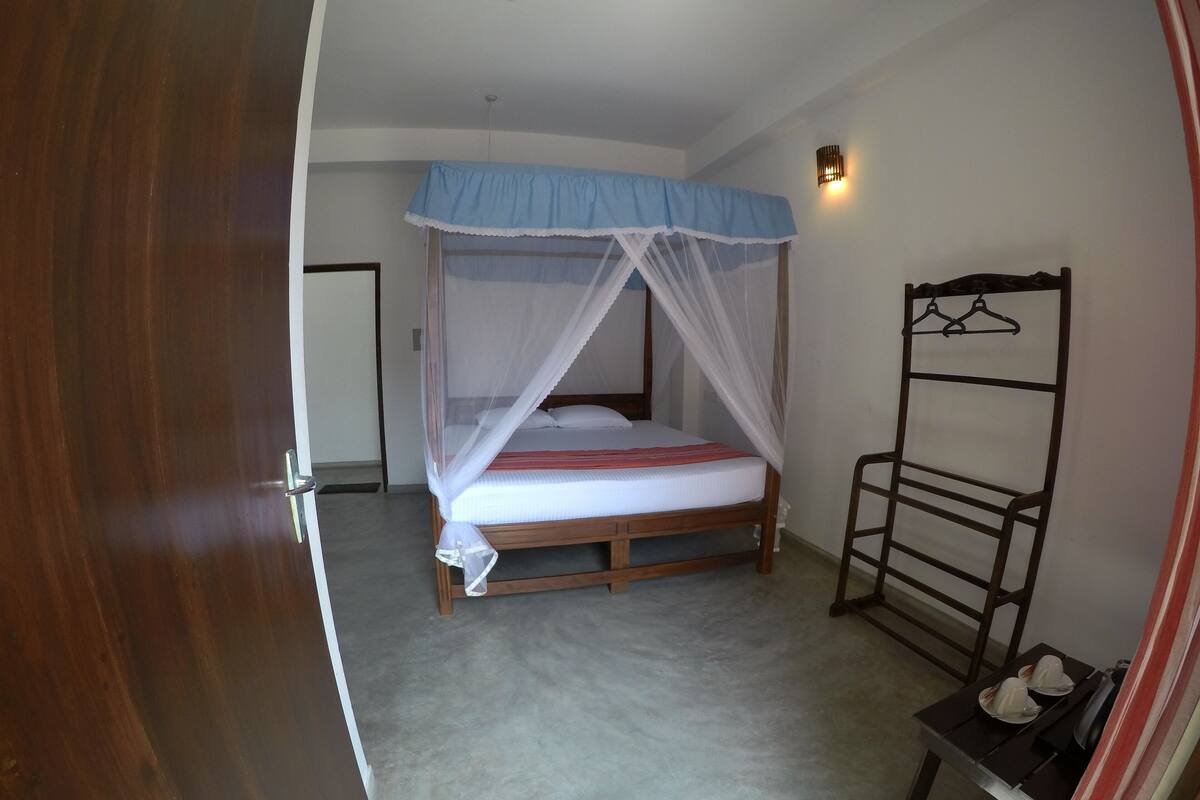 A bedroom with a wooden bed, a canopy, a bedside table with a lamp, and a clothing rack.