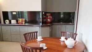 Un comedor con una mesa redonda de madera y cuatro sillas, una tetera blanca y dos tazas blancas sobre la mesa.
