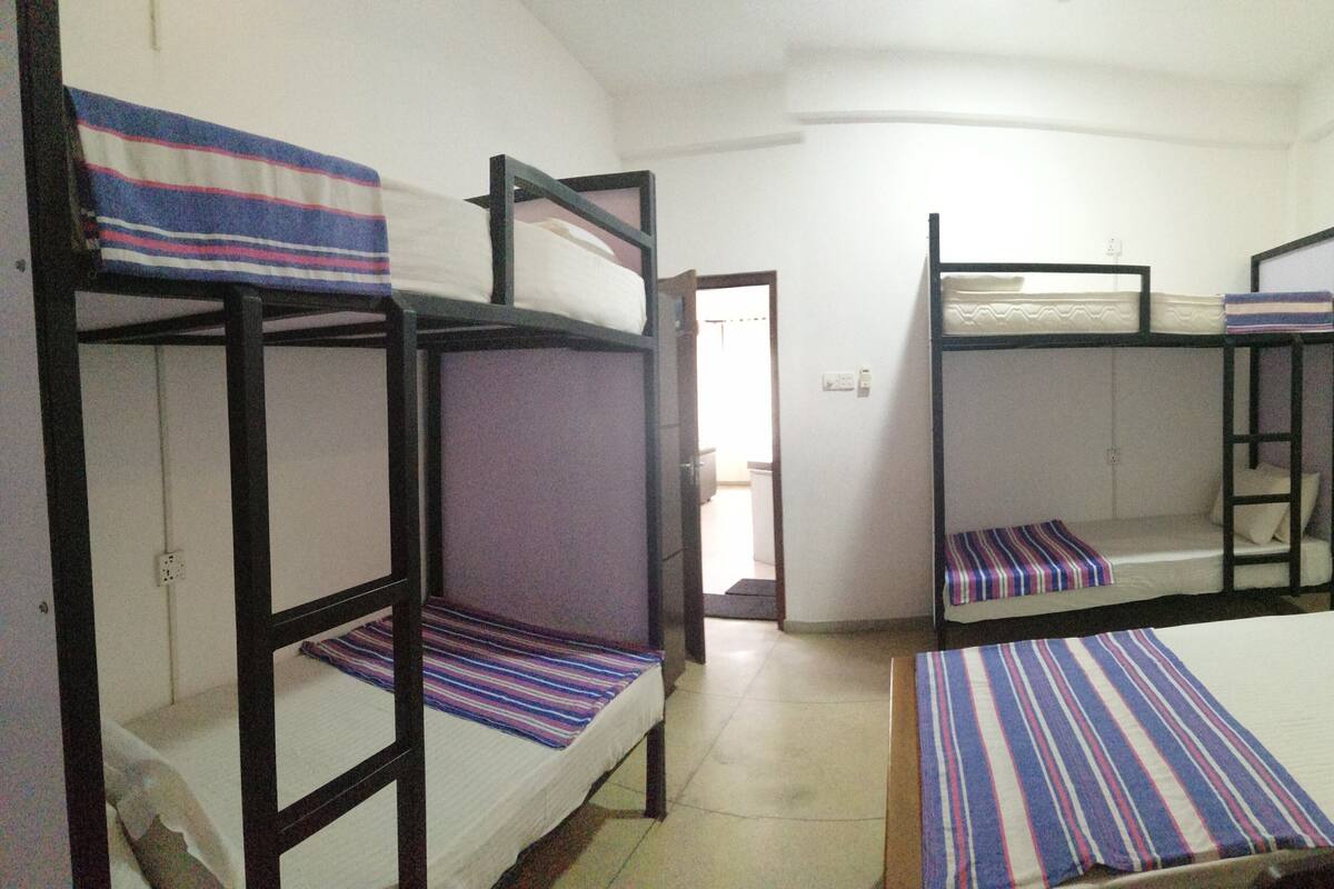 A dormitory room with bunk beds, a door leading to another room, and a tiled floor.