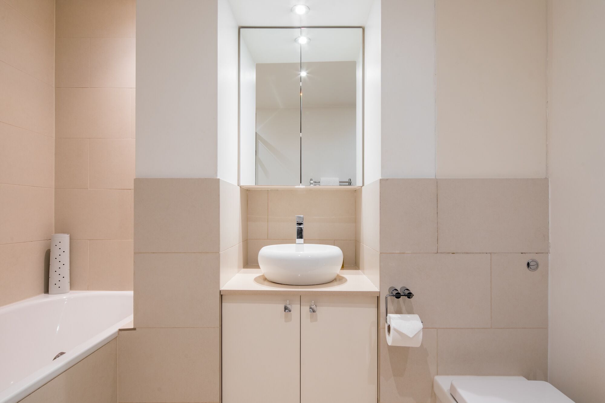 Un baño moderno con un lavamanos blanco, un espejo encima y un inodoro.
