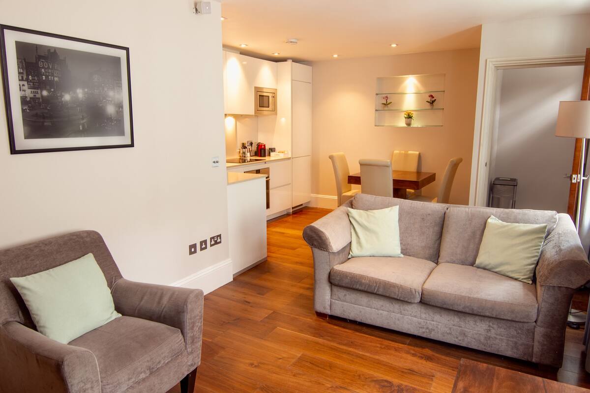A modern living room with a grey sofa, a brown armchair, and a dining area with a table and chairs.