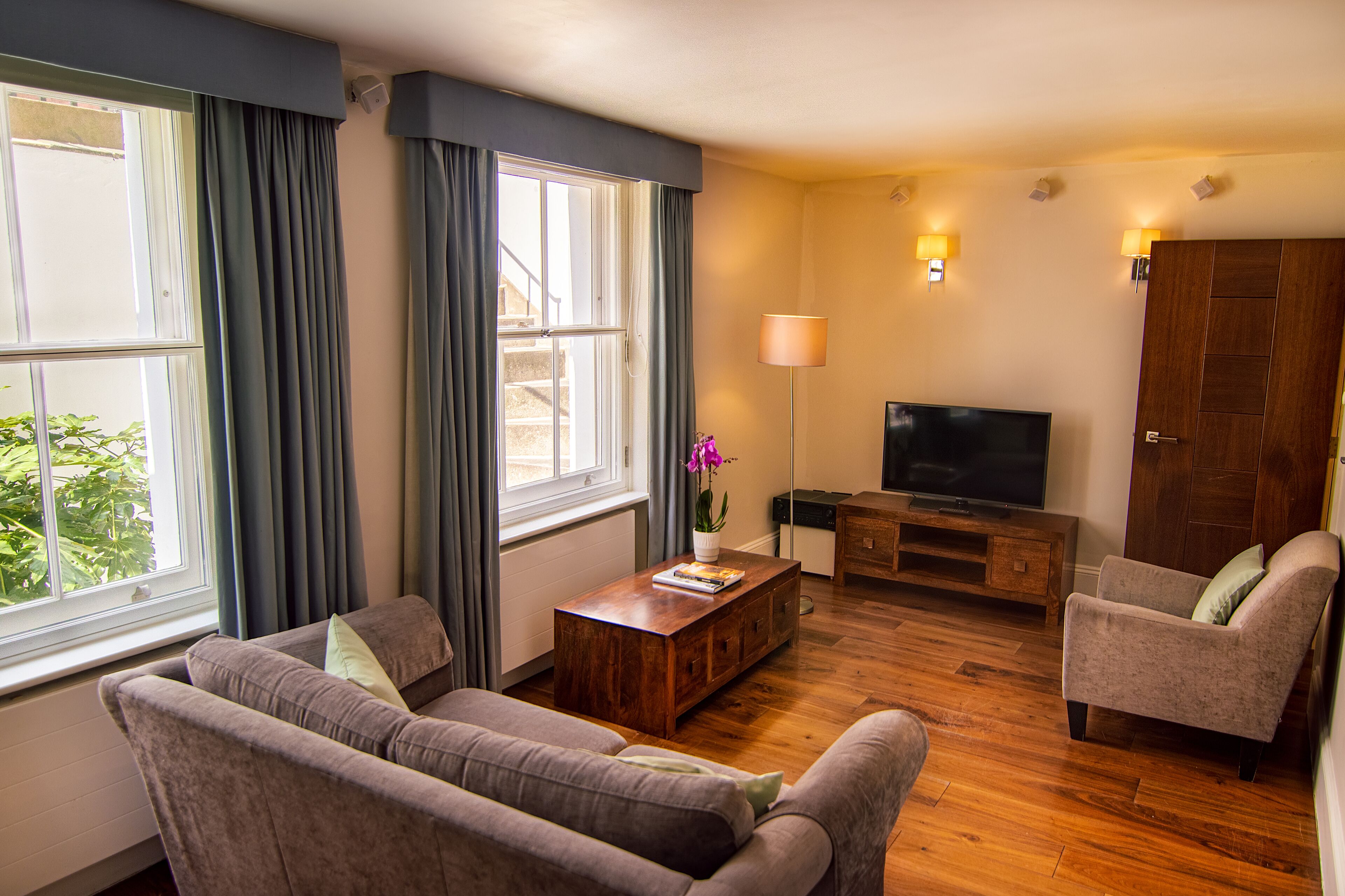 Una sala de estar con sofá, sillón, mesa de centro de madera, televisor y lámpara.