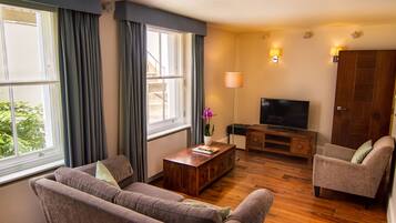 Una sala de estar con sofá, sillón, mesa de centro de madera, televisor y lámpara.