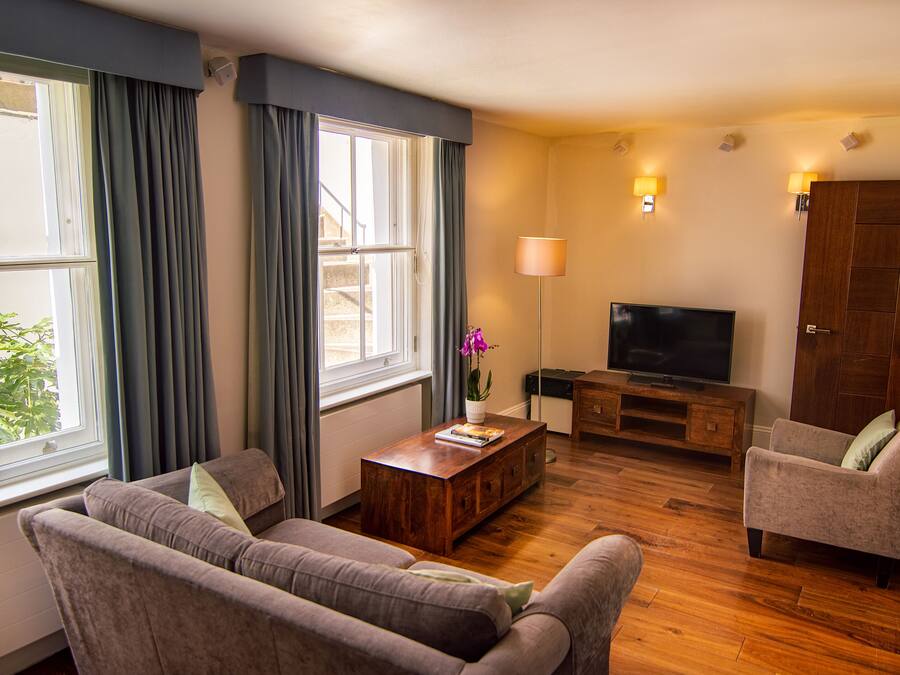 Una sala de estar con sofá, sillón, mesa de centro de madera, televisor y lámpara.