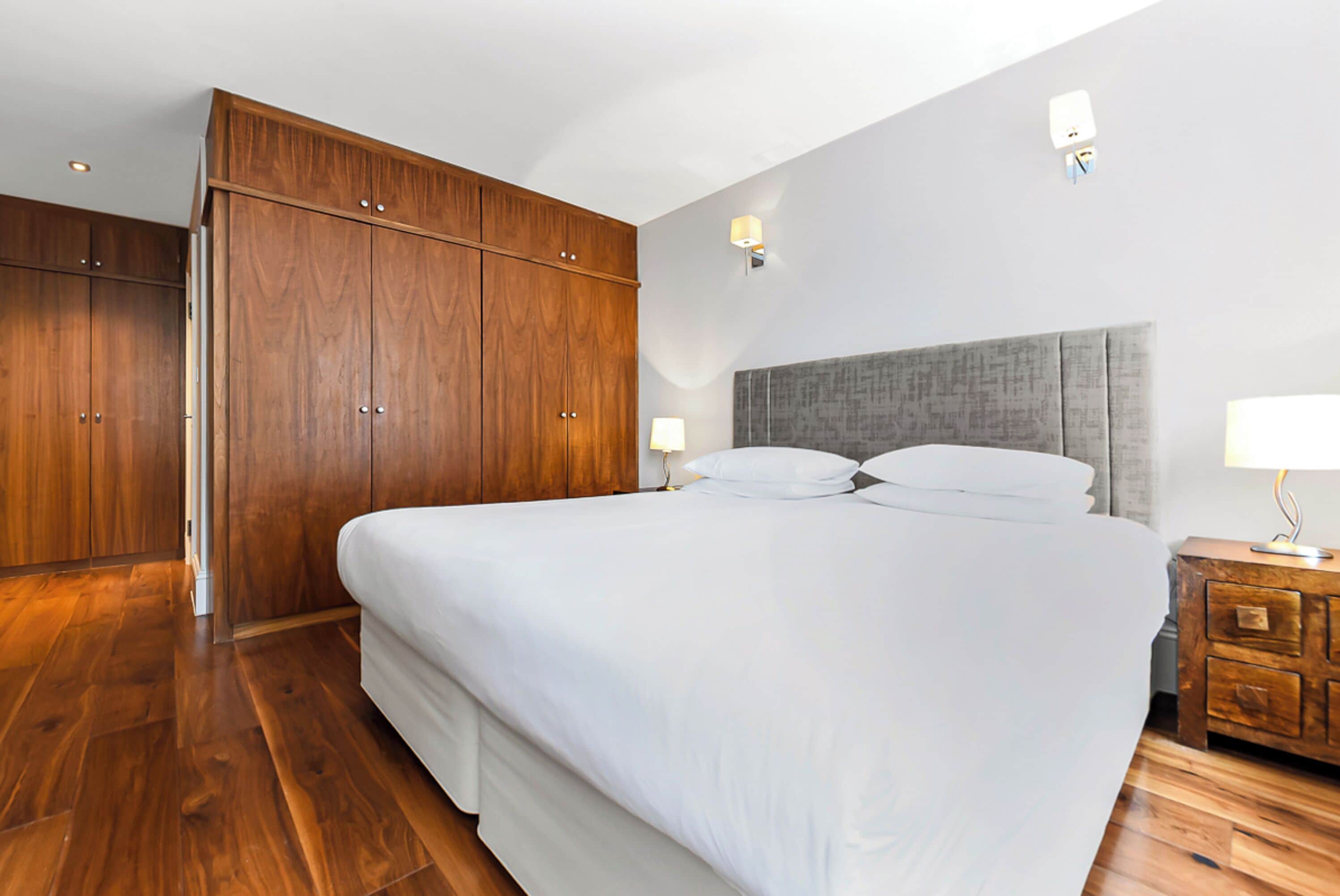 A bedroom with a large bed, wooden wardrobe, and a nightstand with a lamp.