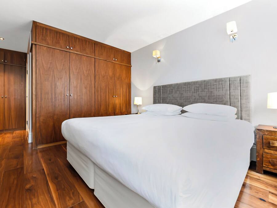 A bedroom with a large bed, wooden wardrobe, and a nightstand with a lamp.