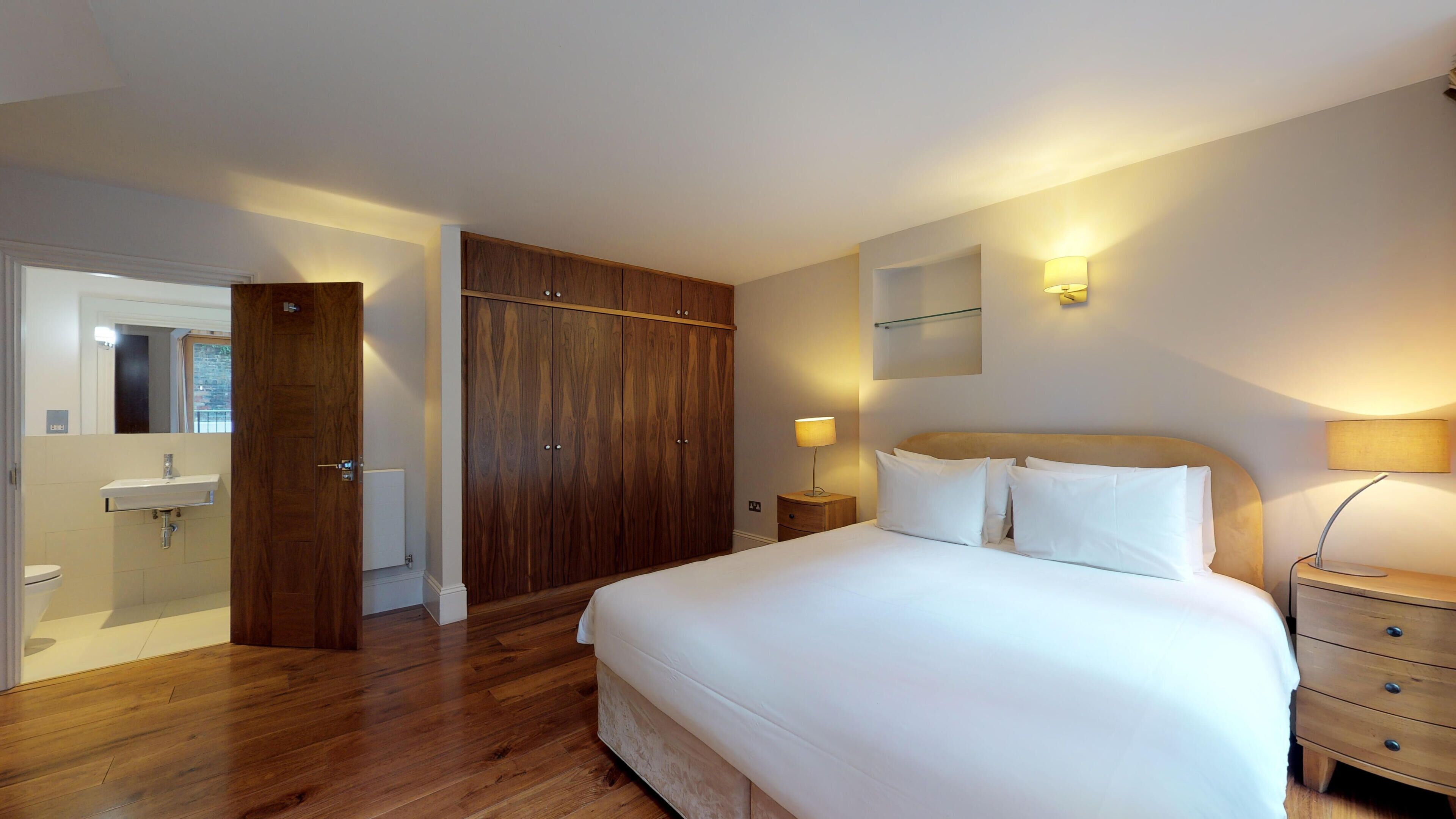 Quarto de hotel com guarda-roupa de madeira, cama com lençóis brancos, mesa de cabeceira com abajur e uma pequena mesa de cabeceira com abajur.