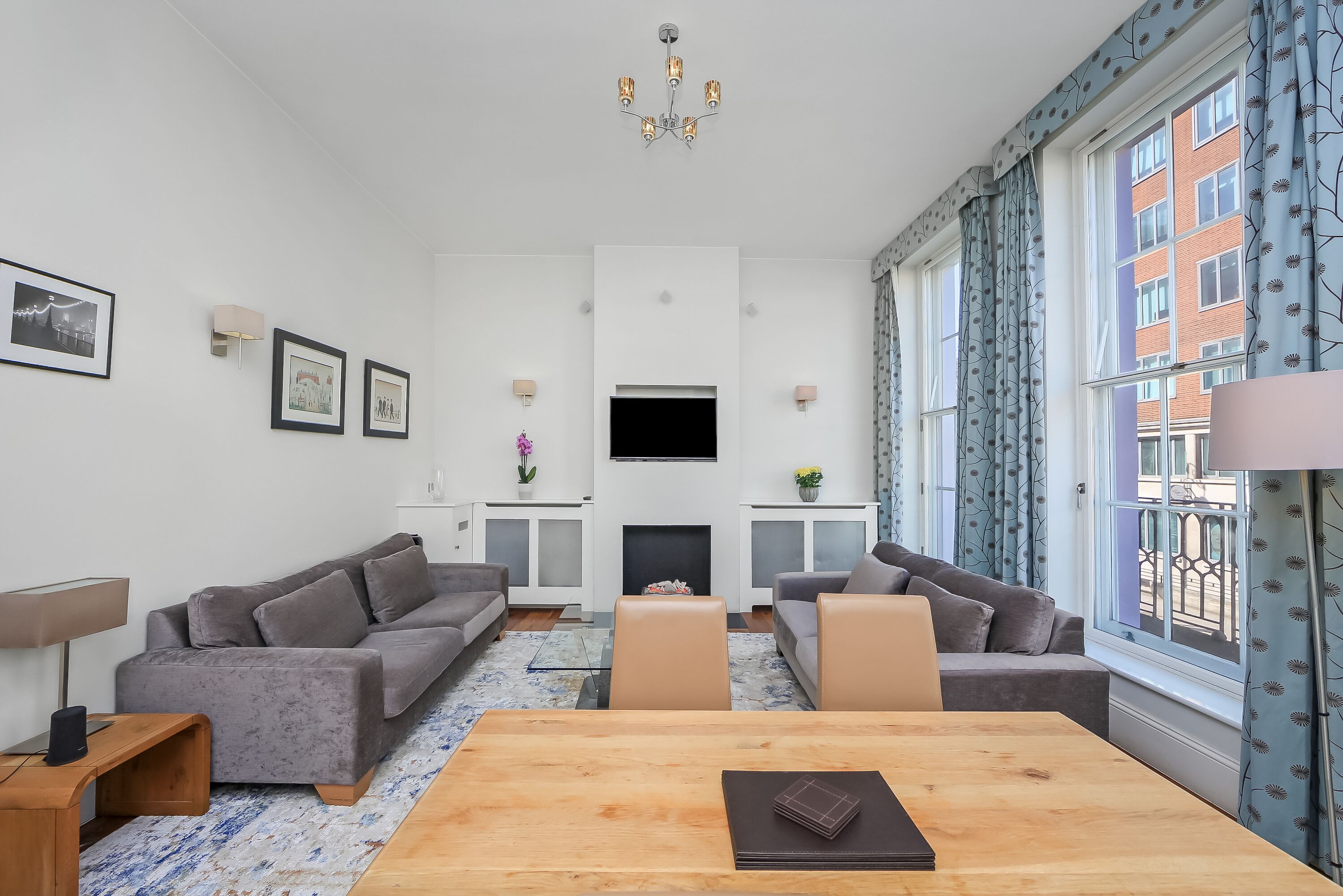 Un salon moderne avec une cheminée, deux canapés, une table basse en bois et de grandes fenêtres ornées de rideaux à motifs.