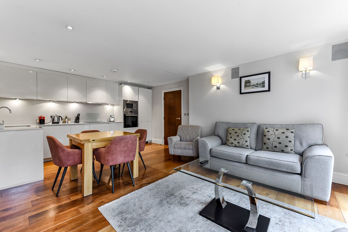 Un espace de vie moderne comprenant une cuisine, un coin repas et un canapé gris agrémenté de coussins à motifs.