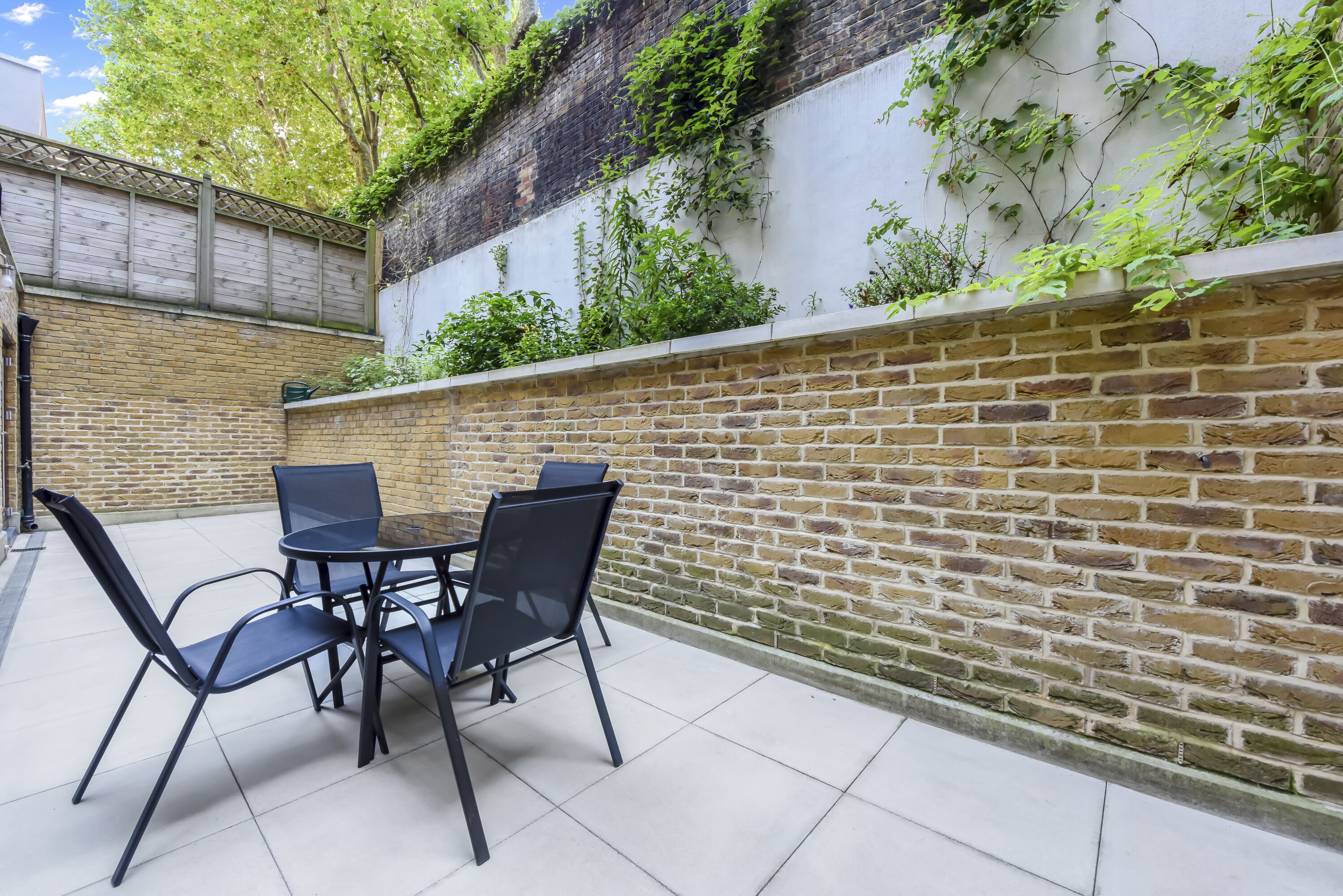 A patio with a brick wall, a table with chairs, and a small garden area with plants growing on the wall.