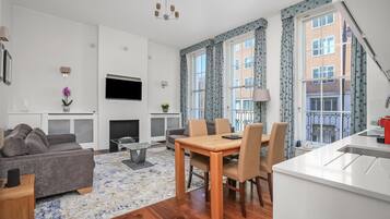 Una sala de estar moderna con un sofá gris, una mesa de comedor de madera y una cocina con encimera blanca.
