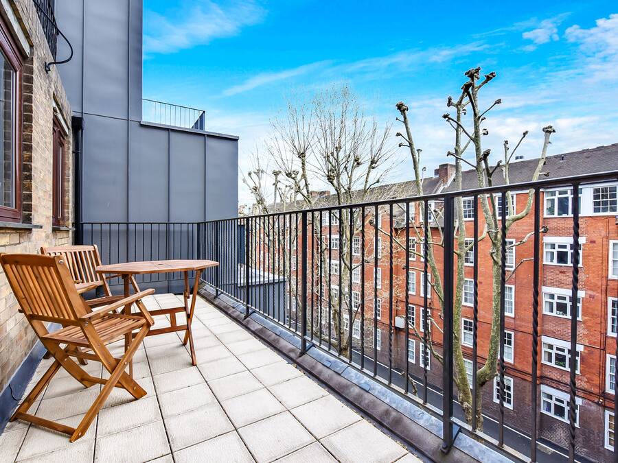 A balcony with a table and chairs, overlooking a brick building and trees.