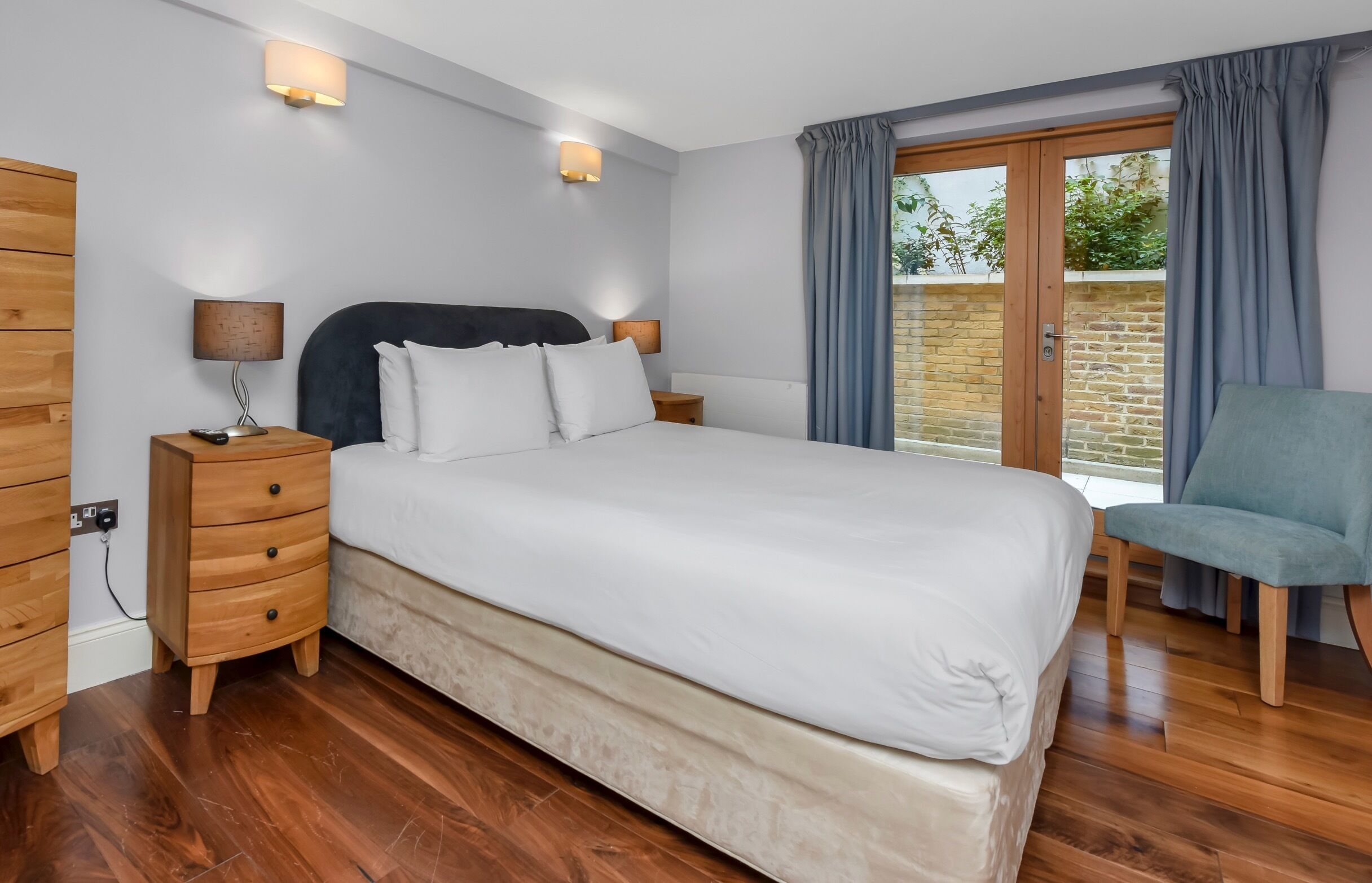 A bedroom with a large bed, wooden nightstands, a chair, and a view of the outdoors through a sliding glass door.