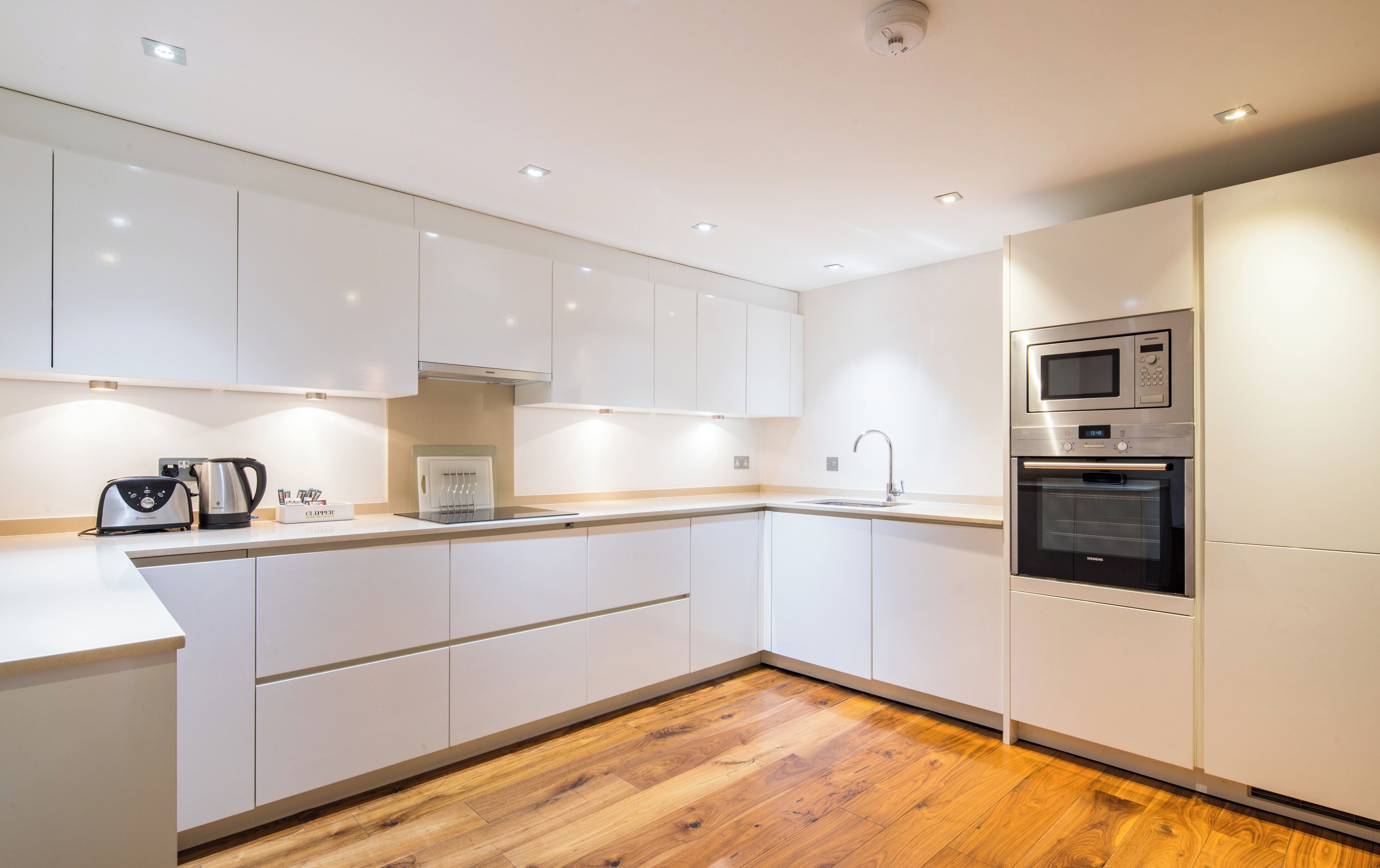Una cocina moderna con armarios blancos, suelo de madera, horno empotrado y microondas.