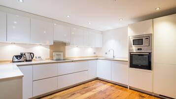 Una cocina moderna con armarios blancos, suelo de madera, horno empotrado y microondas.
